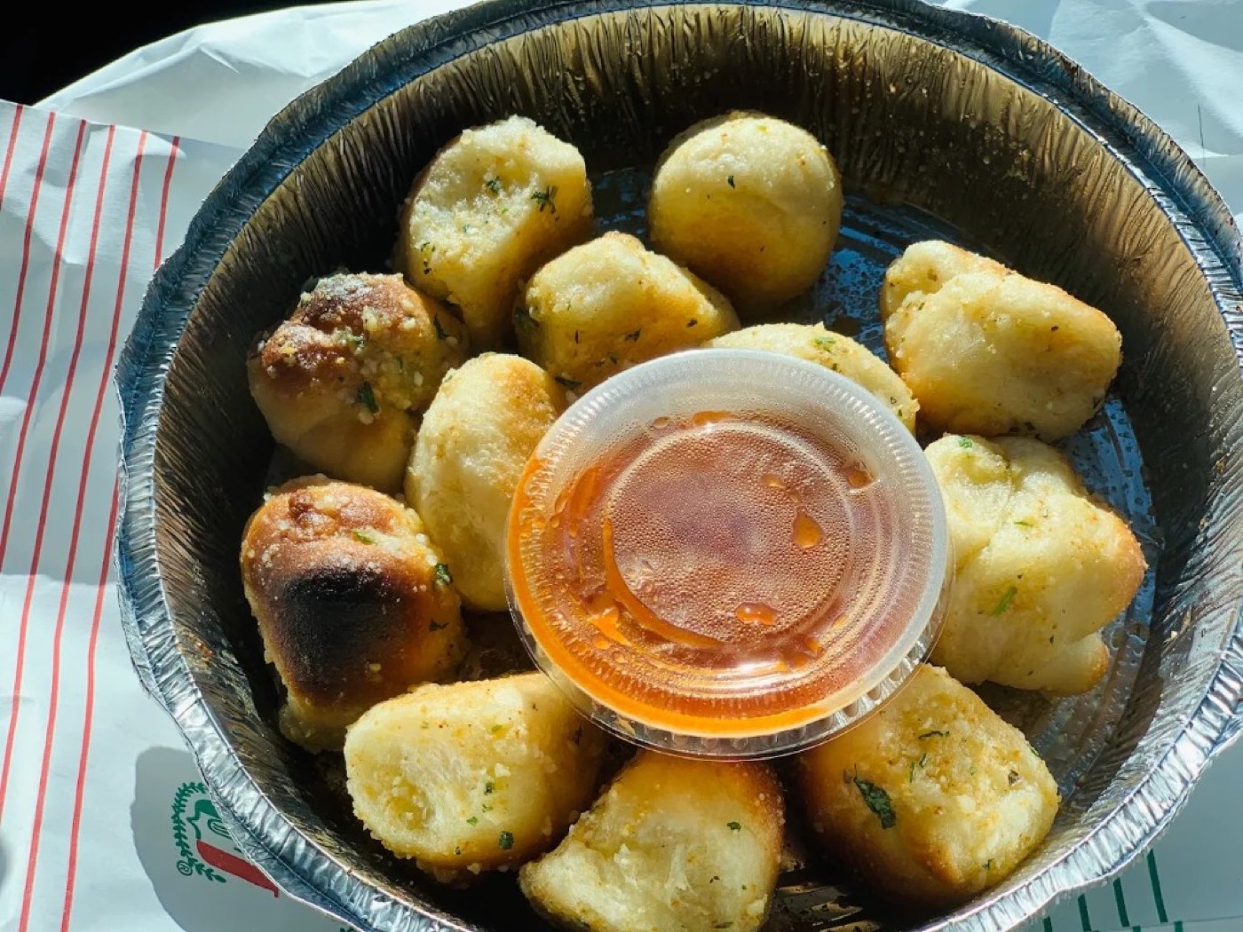 Garlic knots in a round pan with a cup of marinara.