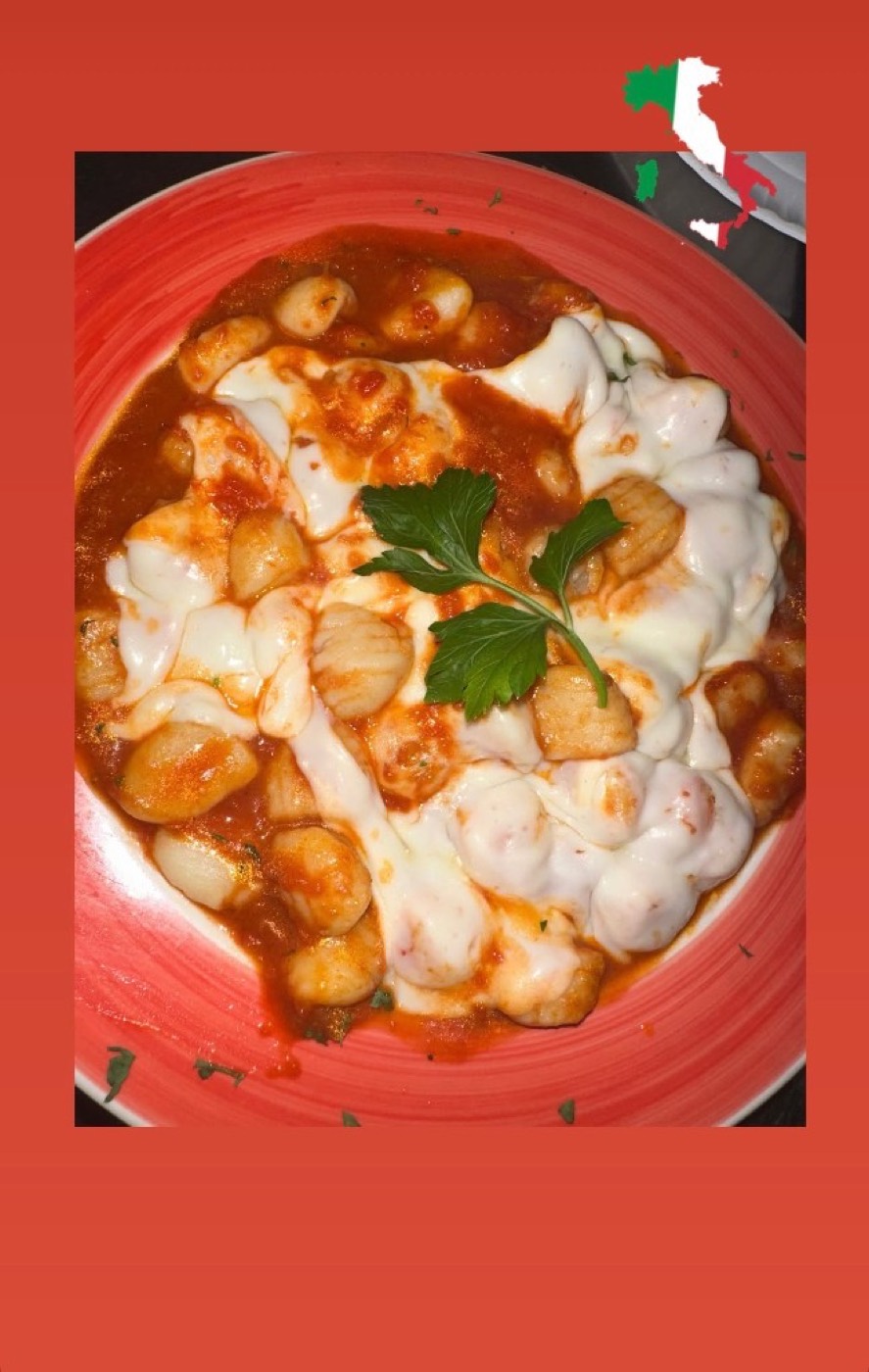Gnocchi in red sauce under melted mozzarella, with a parsley sprig.
