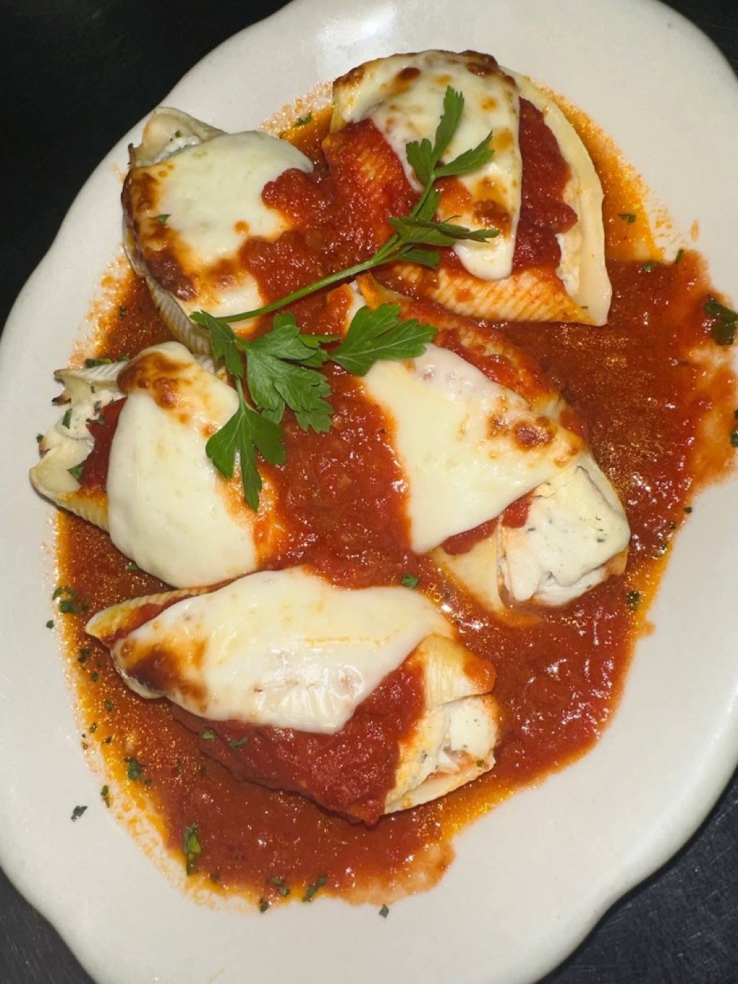 Four stuffed shells in tomato sauce topped with melted mozzarella.